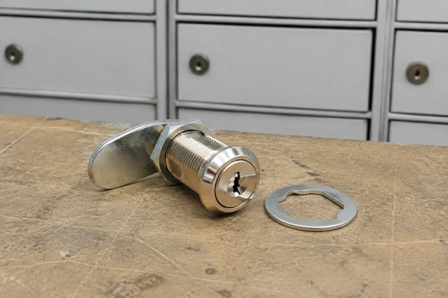 Detached threaded cam lock and mounting washer on a workbench in front of closed mail compartments. — Mailbox Lock Replacement, Caledon